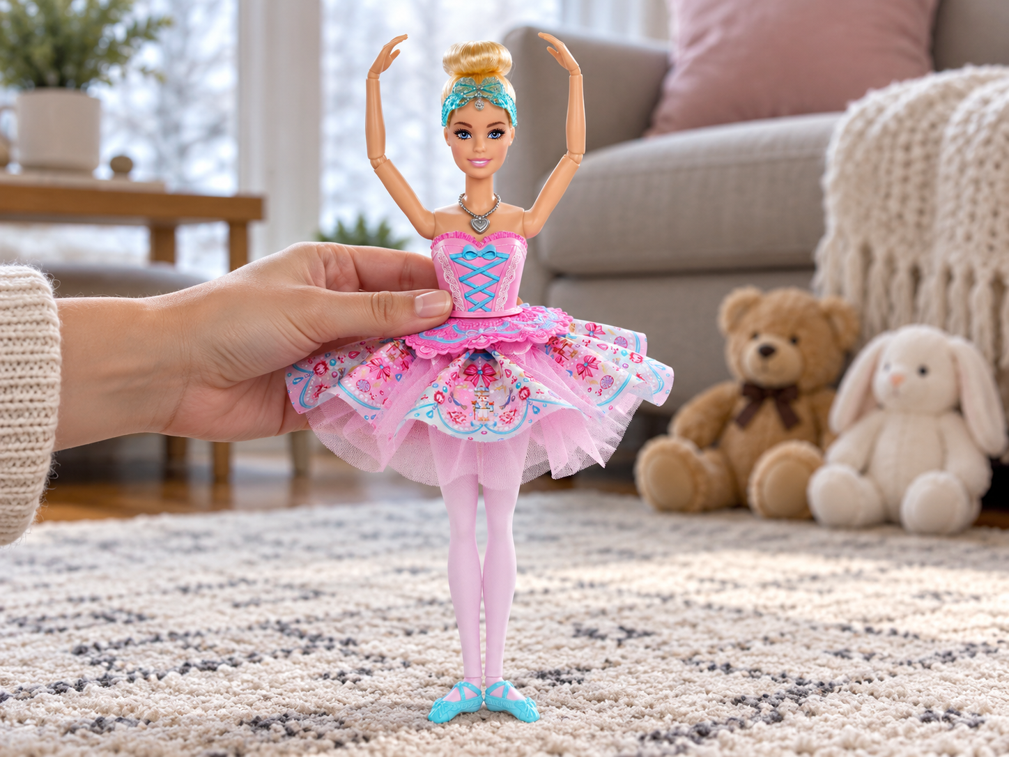 Una mano tiene la bambola Barbie Clara in posa da balletto davanti a un pubblico di peluche.