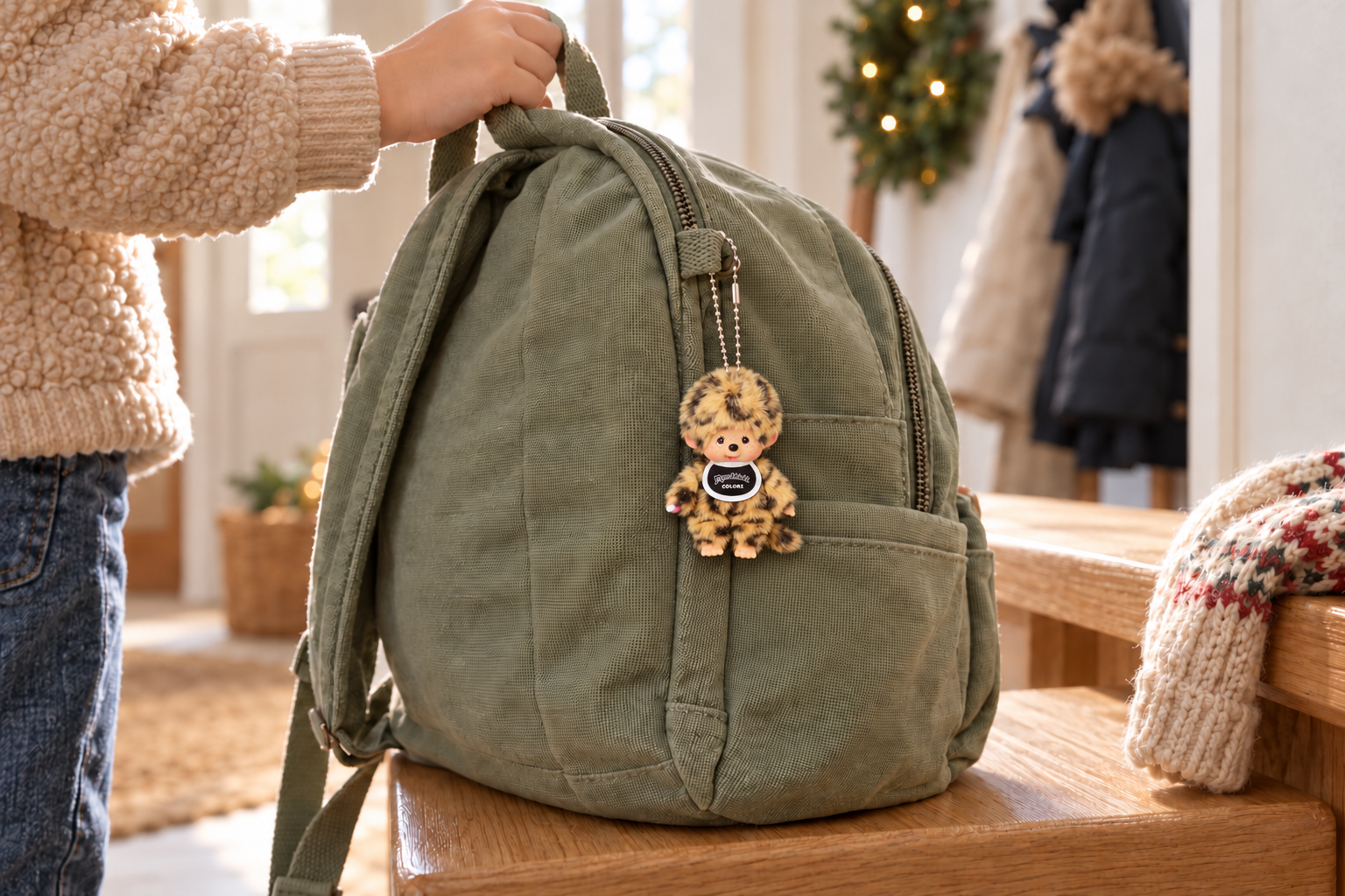 Leopard privjesak Monchhichi obješen na zelenom dječjem ruksaku.